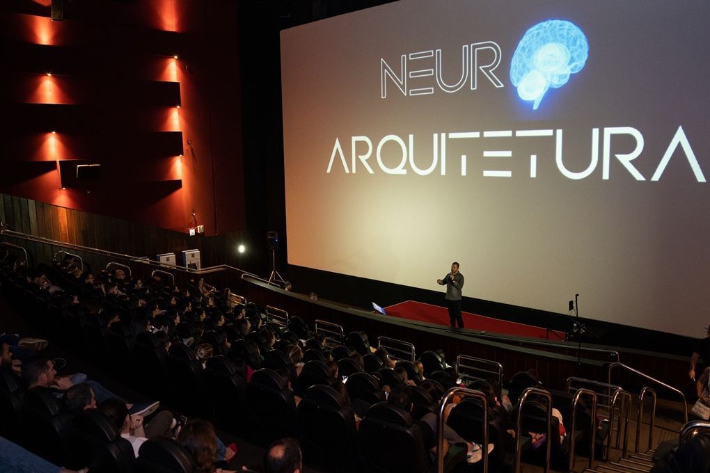 Um homem está fazendo uma apresentação em frente a uma tela grande que diz neuro arquitectura