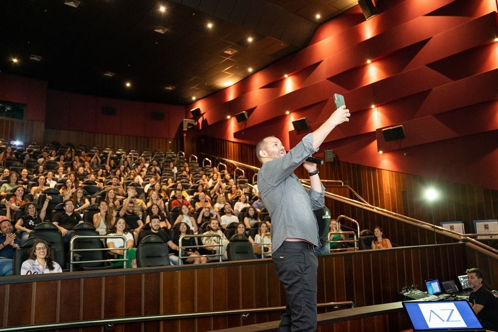Um homem está tirando uma selfie na frente de uma plateia em um teatro.