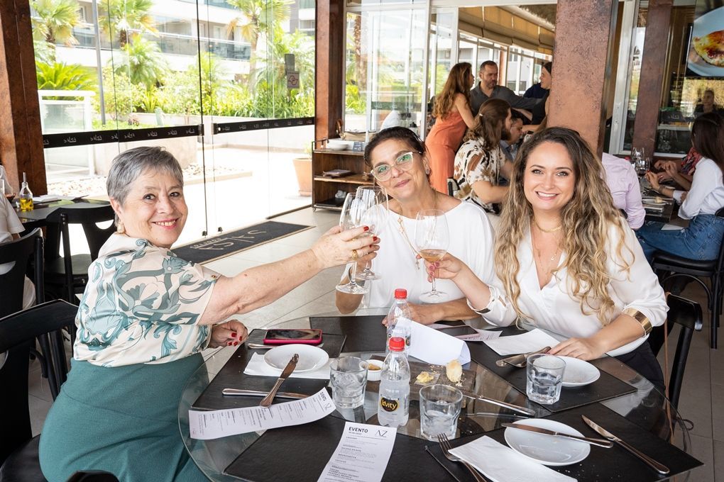 Três mulheres estão sentadas à mesa de um restaurante brindando com taças de vinho.