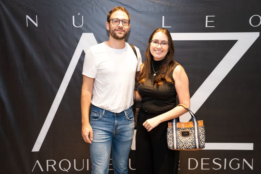 Um homem e uma mulher estão posando para uma foto em frente a uma placa que diz design
