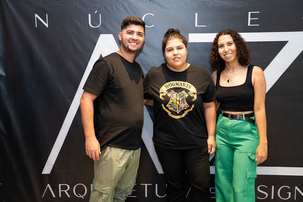 Um homem e duas mulheres estão posando para uma foto em frente a uma placa.