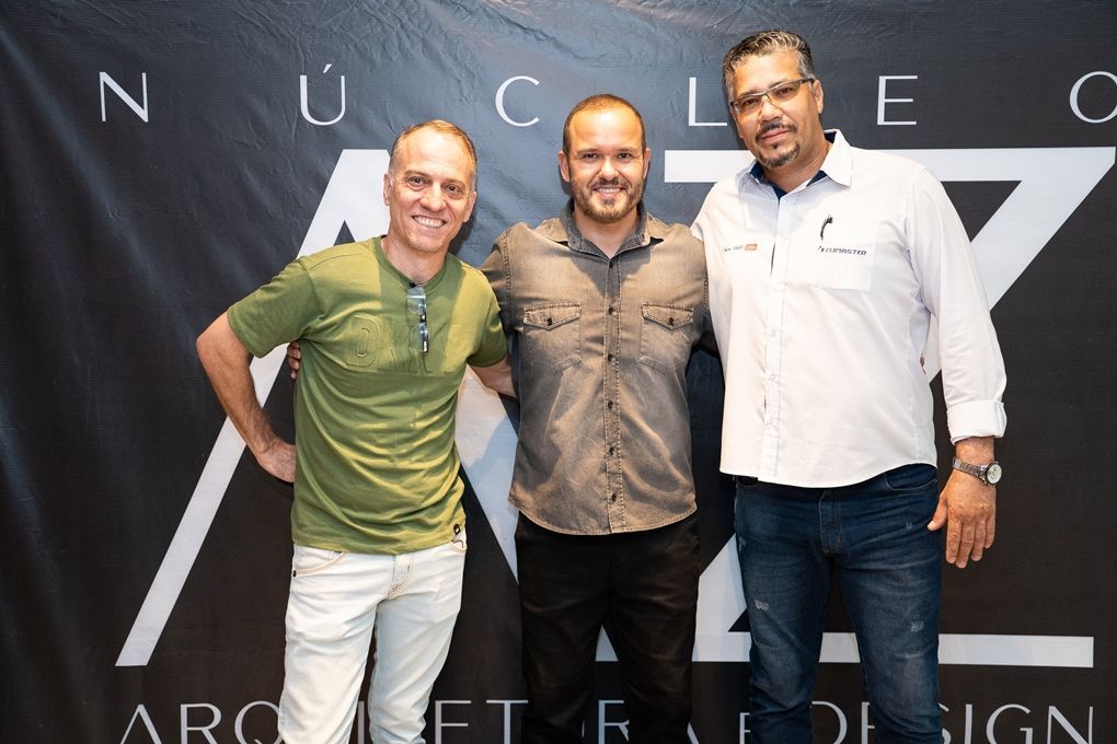 Três homens estão posando para uma foto em frente a uma placa que diz nucleo