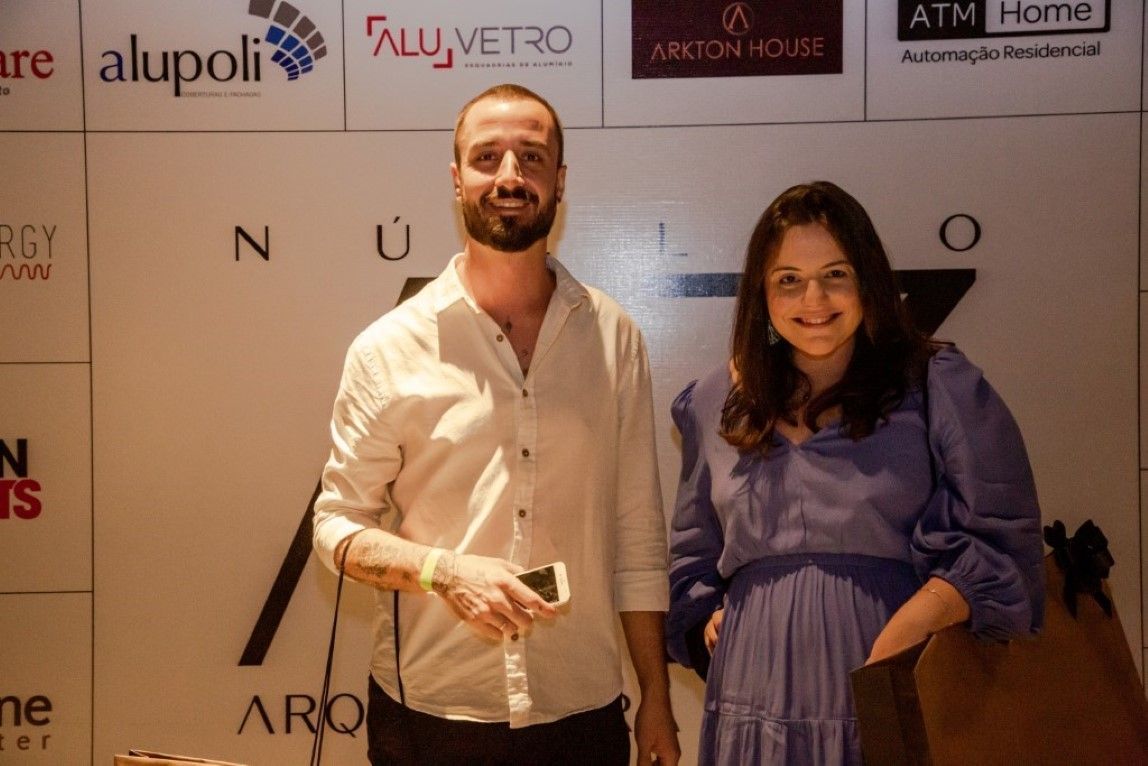 Um homem e uma mulher estão posando para uma foto em frente a uma parede com logotipos.