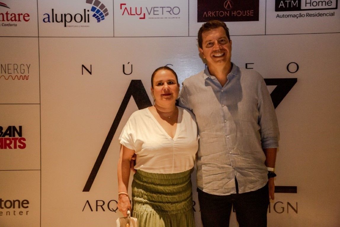 Um homem e uma mulher estão posando para uma foto em frente a uma parede com logotipos.