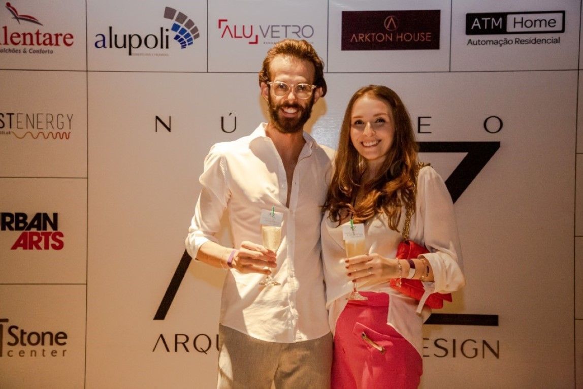 Um homem e uma mulher estão posando para uma foto em frente a uma parede com logotipos.
