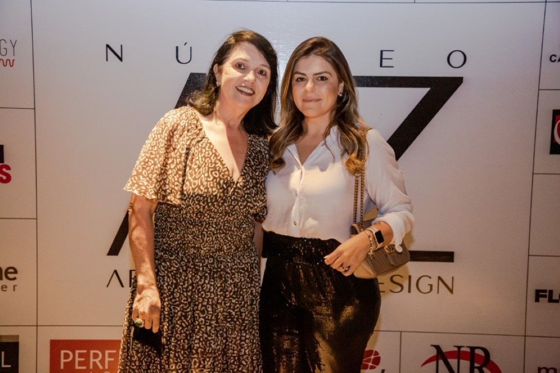 Duas mulheres estão posando para uma foto em frente a uma placa que diz neo