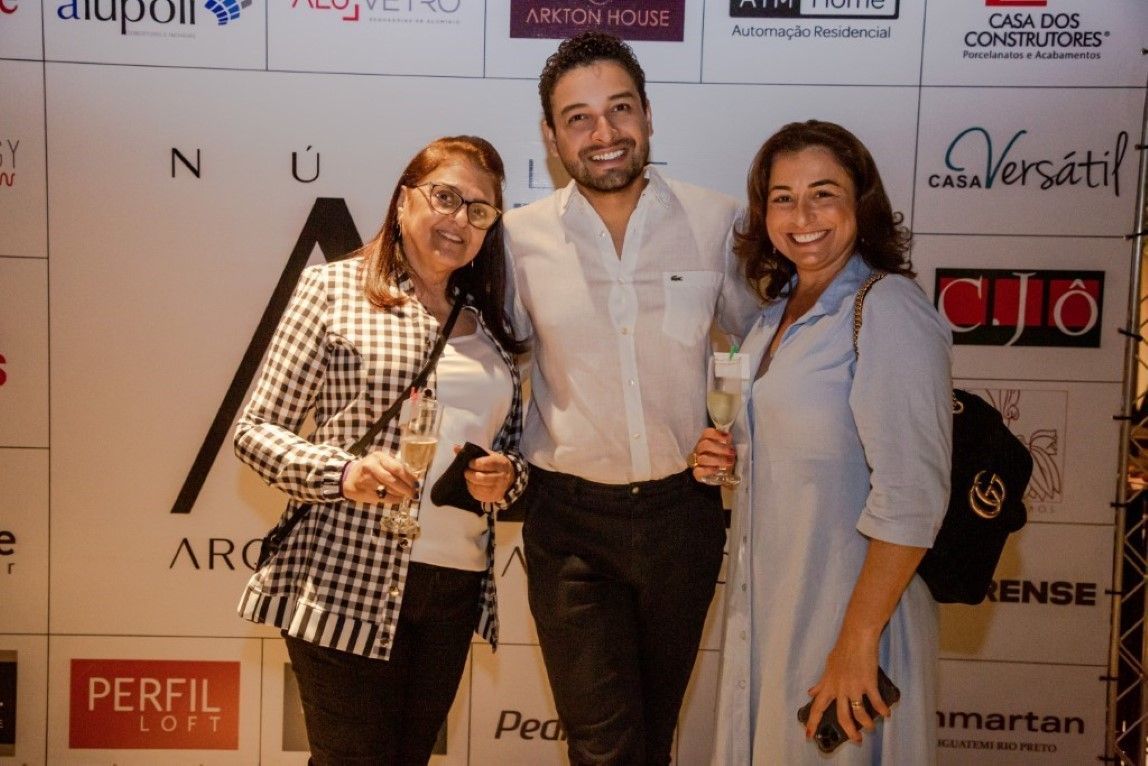 Um homem e duas mulheres estão posando para uma foto em frente a uma parede com logotipos.
