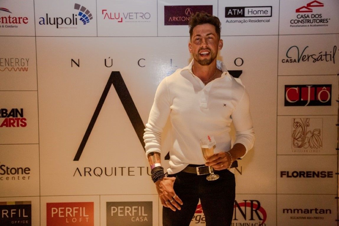 Um homem de camisa branca está parado em frente a uma parede com logotipos.