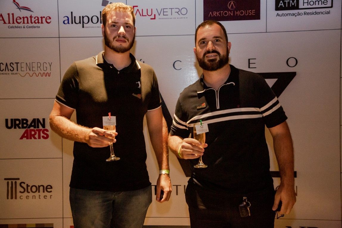 Dois homens estão de pé, um ao lado do outro, segurando taças de vinho.