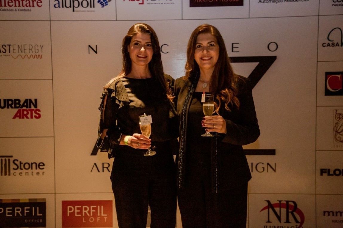 Duas mulheres em pé uma ao lado da outra em frente a uma parede que diz perfil