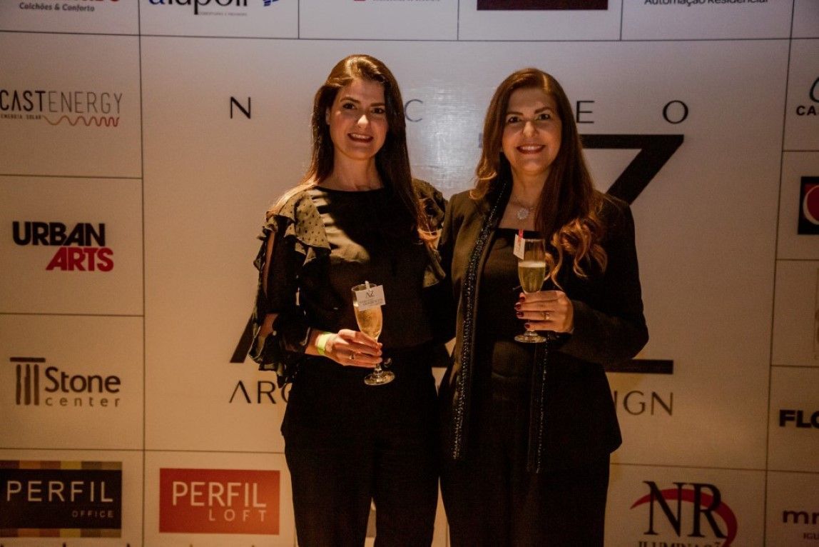 Duas mulheres em pé em frente a uma parede com logotipos de artes urbanas e perfil