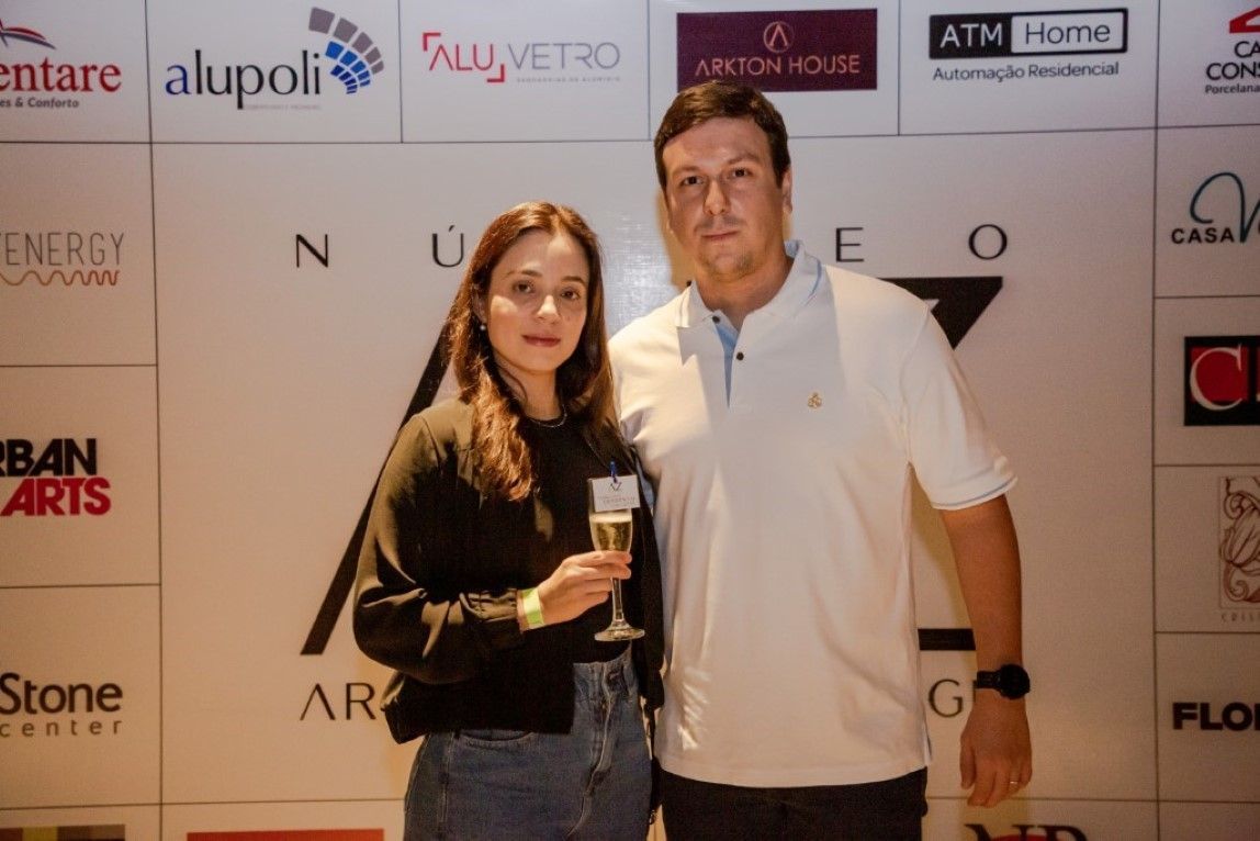 Um homem e uma mulher estão posando para uma foto em frente a uma parede com logotipos.