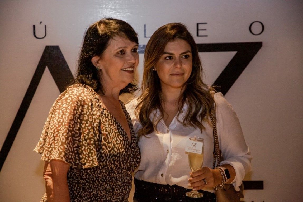 Duas mulheres estão posando para uma foto e uma delas está segurando uma taça de champanhe.