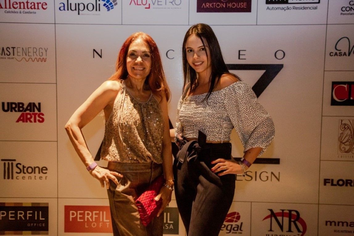 Duas mulheres estão posando para uma foto em frente a uma parede com logotipos.