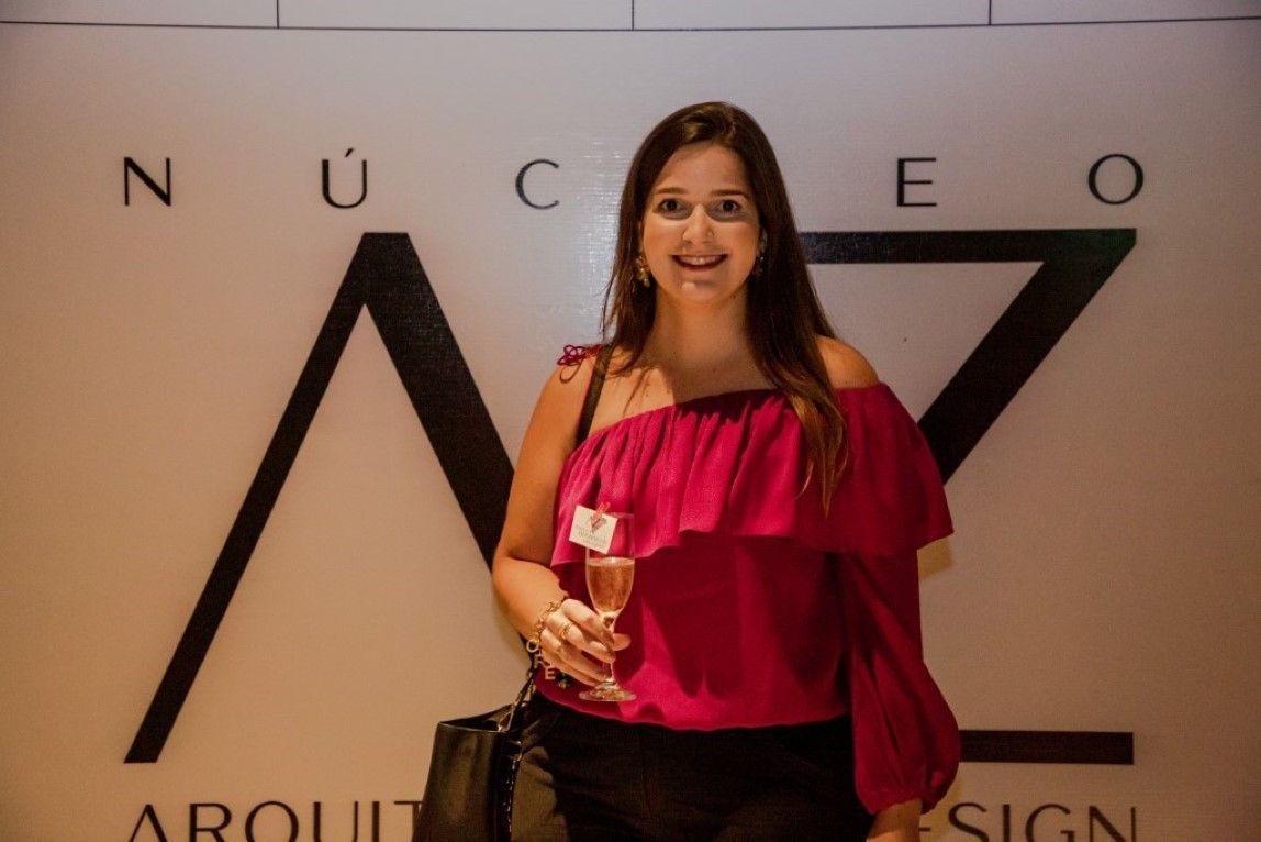 Uma mulher com uma blusa rosa está parada em frente a uma placa que diz nuceo