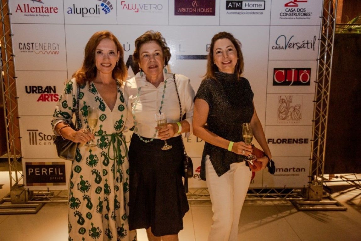 Três mulheres estão posando para uma foto em frente a uma parede com logotipos.