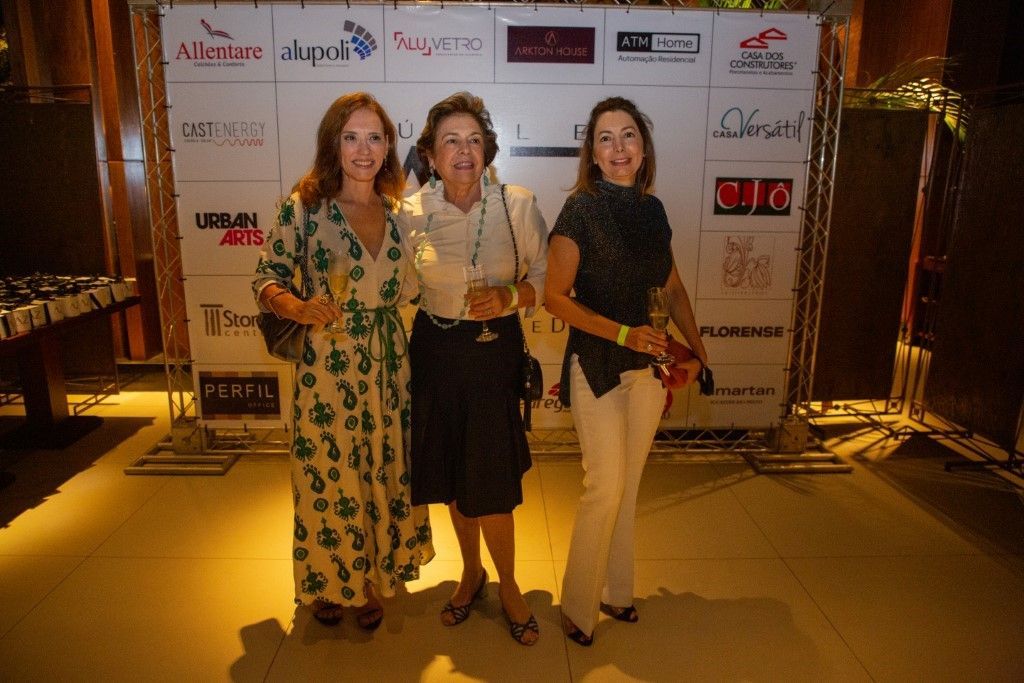 Três mulheres estão posando para uma foto em frente a uma parede com logotipos