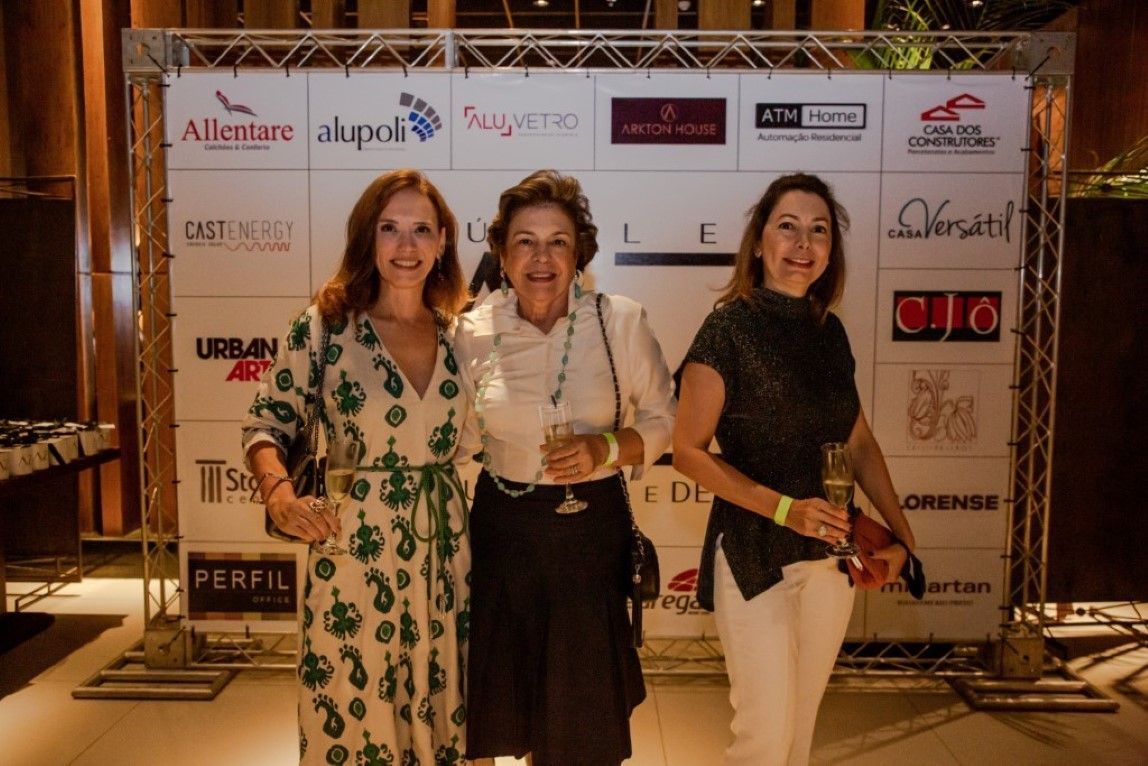 Três mulheres estão posando para uma foto em frente a uma parede com logotipos.