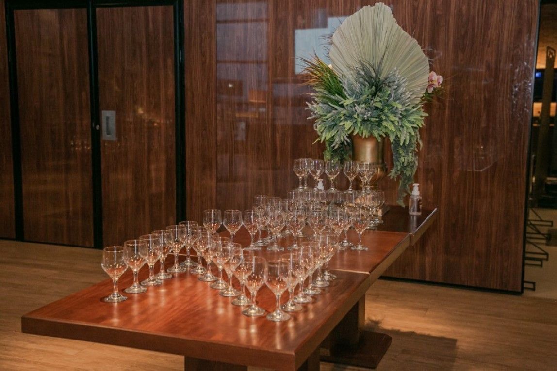 Uma mesa de madeira coberta com muitas taças de vinho e um vaso de flores.