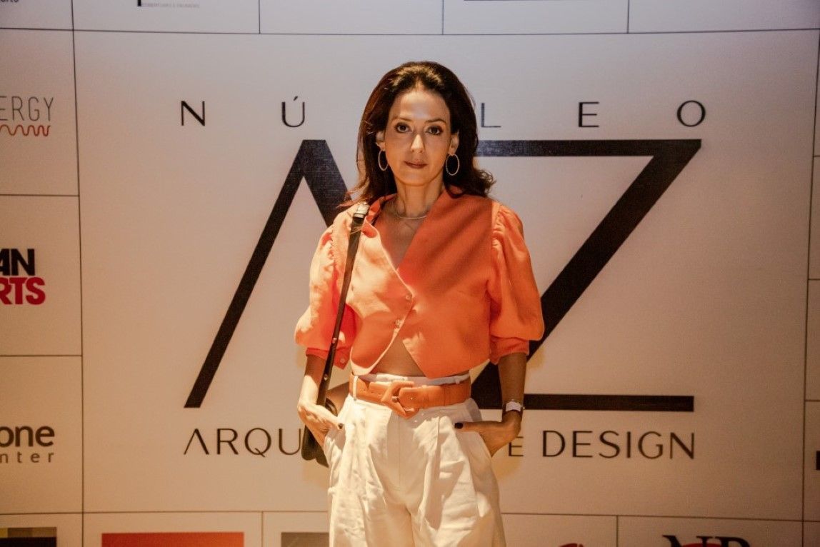 Uma mulher de camisa laranja e calça branca está parada em frente a uma placa que diz design.