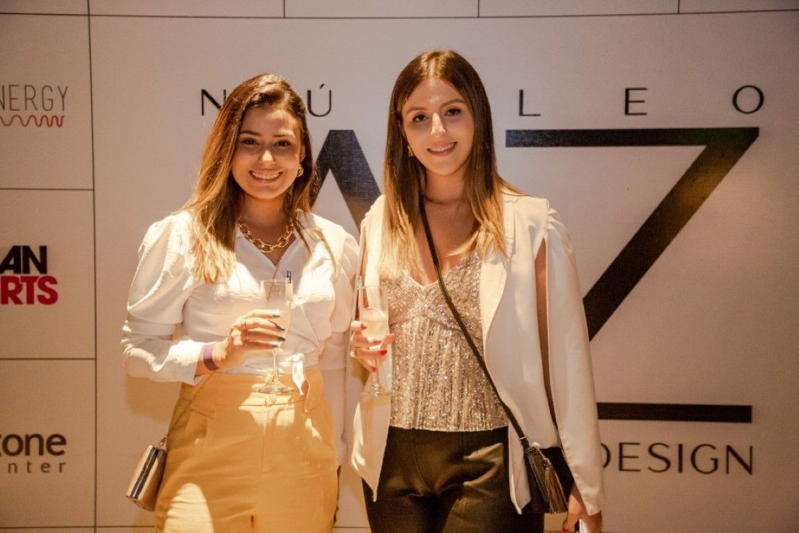 Duas mulheres estão posando para uma foto em frente a uma placa que diz design.