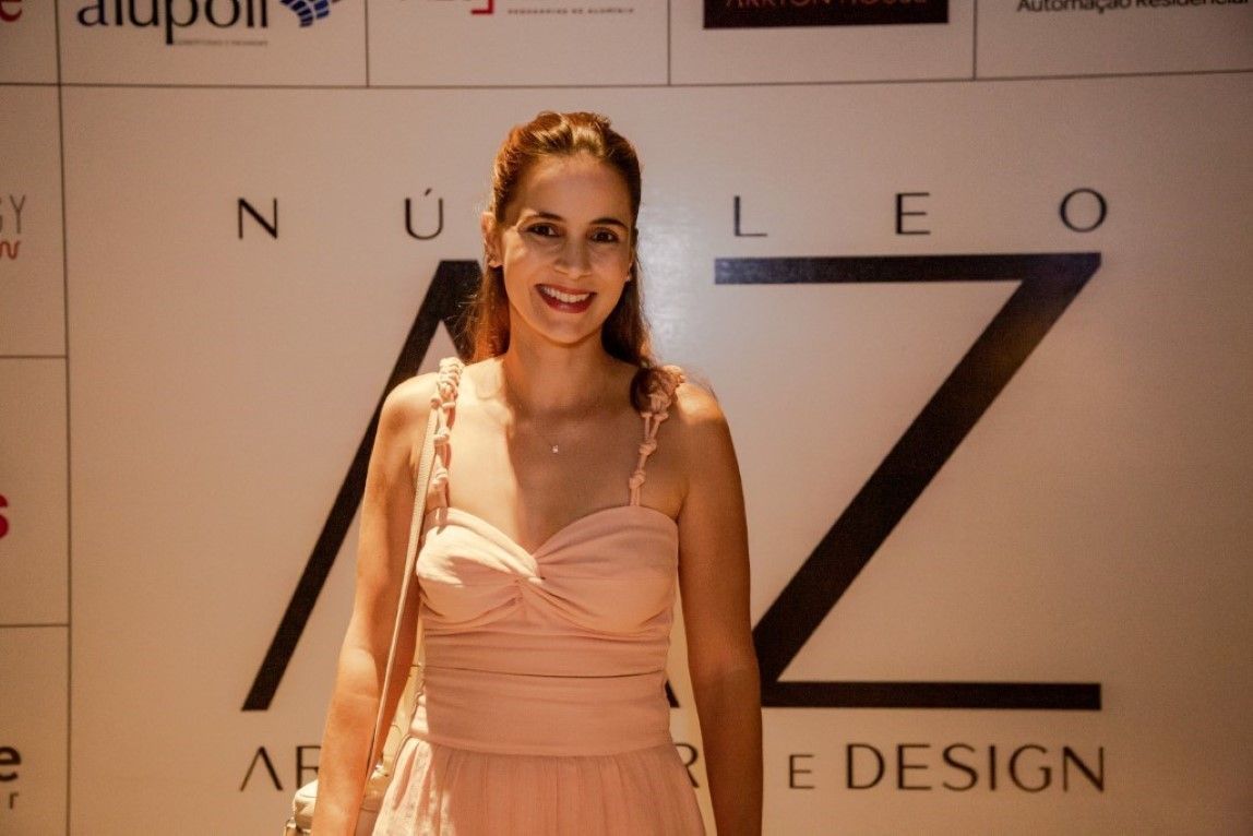Uma mulher de vestido rosa está em frente a uma parede com a letra z escrita nela