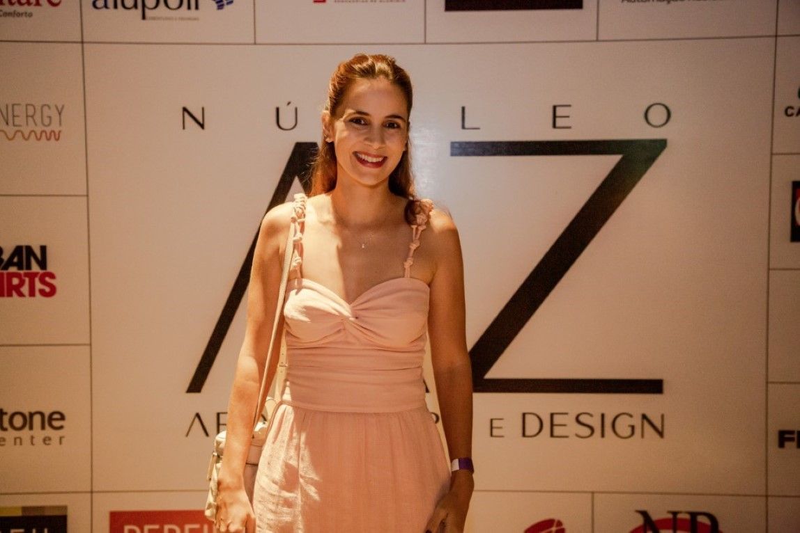 Uma mulher com um vestido rosa está parada em frente a uma parede com a letra z escrita nela.