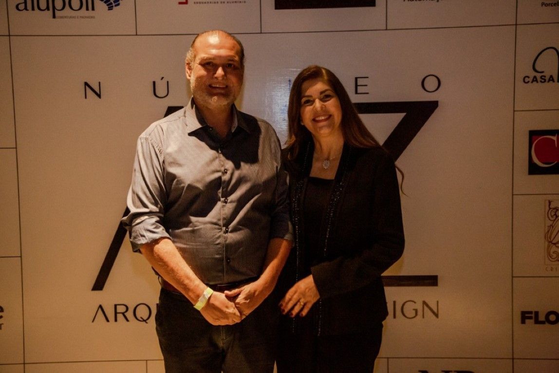 Um homem e uma mulher estão posando para uma foto em frente a uma parede com logotipos.