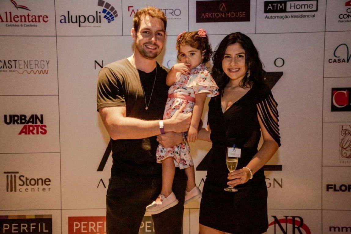 Um homem e uma mulher segurando uma menina em frente a uma parede com logotipos de artes urbanas
