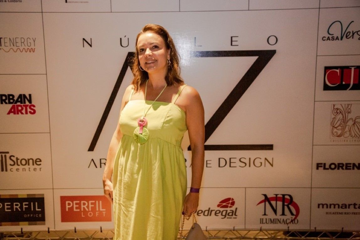 Uma mulher com um vestido verde está parada em frente a uma parede com logotipos
