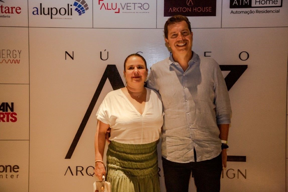 Um homem e uma mulher estão posando para uma foto em frente a uma parede com logotipos.