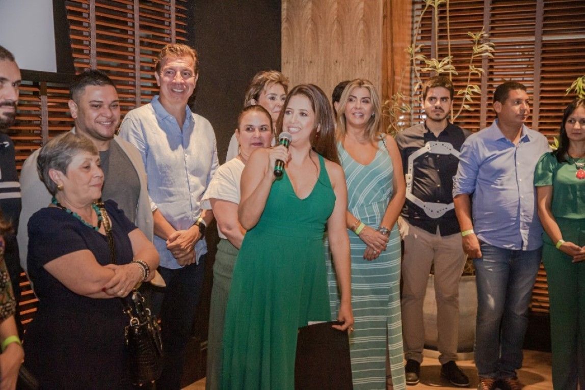 Um grupo de pessoas está em volta de uma mulher de vestido verde segurando um microfone.