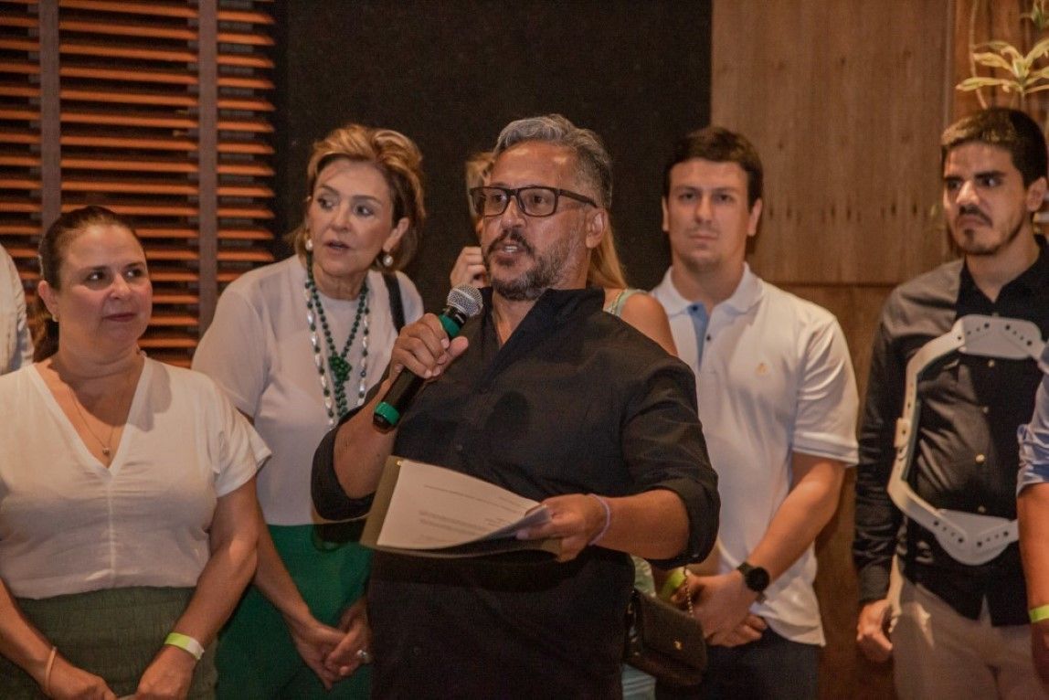 Um homem está falando em um microfone enquanto está em frente a um grupo de pessoas.