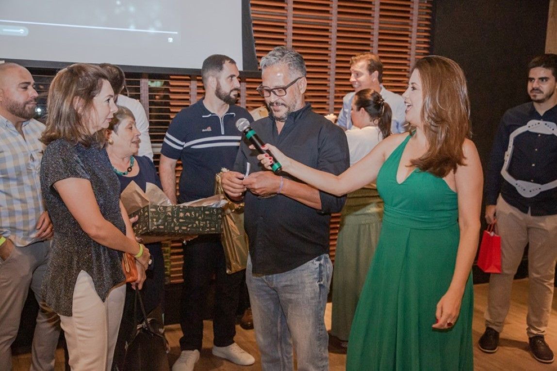 Um grupo de pessoas está em volta de uma mulher de vestido verde segurando um microfone.
