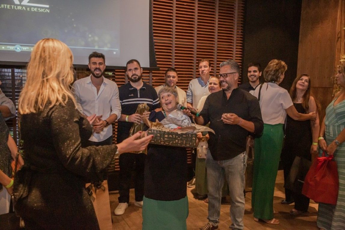 Um grupo de pessoas está em volta de uma mulher segurando uma caixa de presente.