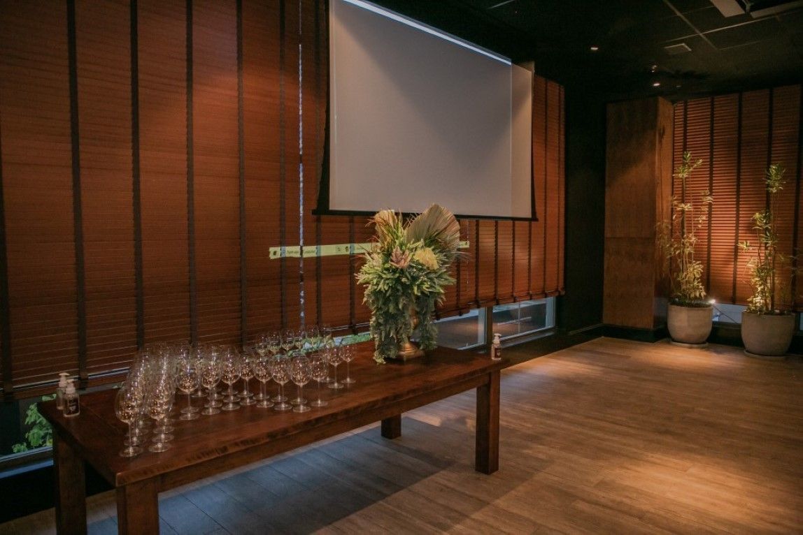 Uma mesa de madeira com taças de vinho em frente a uma tela de projetor.