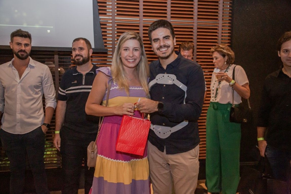 Um homem e uma mulher estão posando para uma foto na frente de um grupo de pessoas.