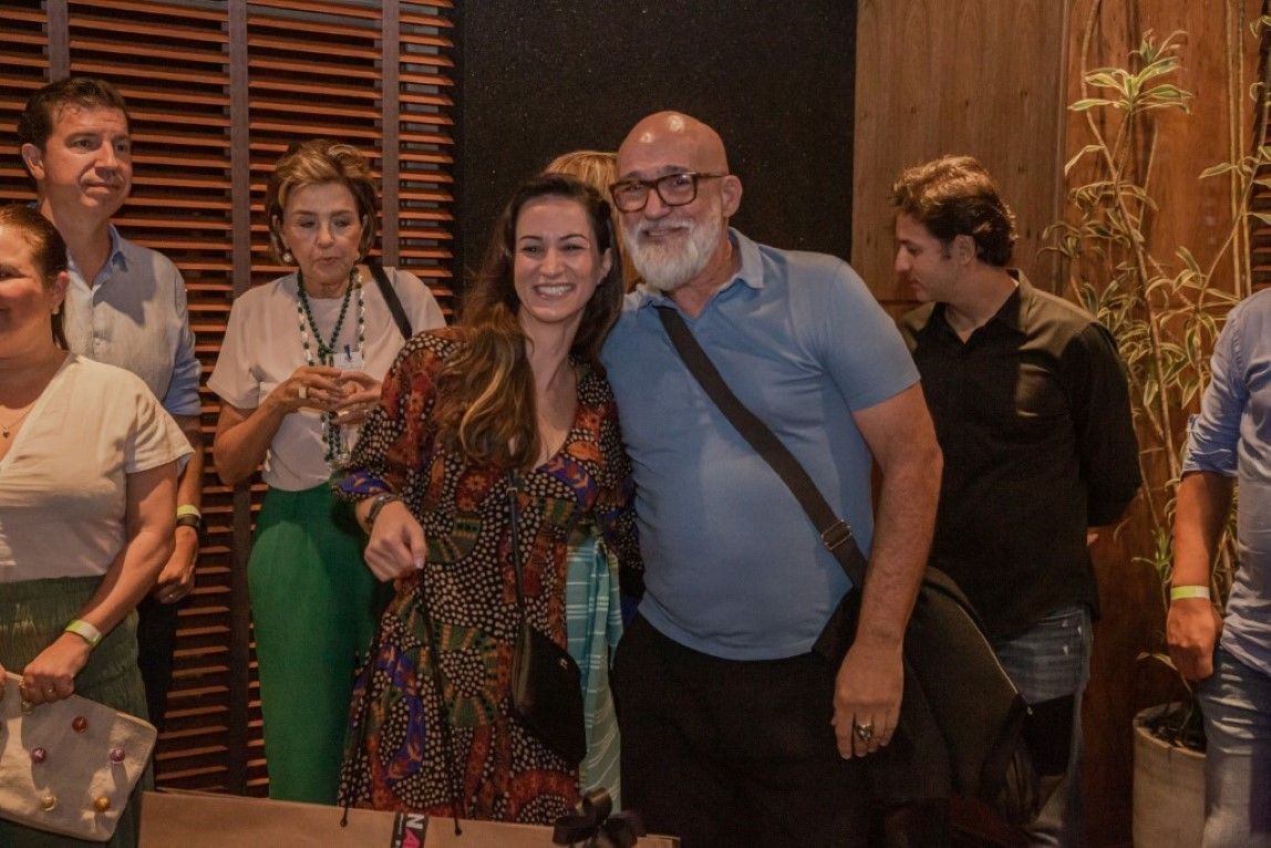 Um homem e uma mulher estão posando para uma foto na frente de um grupo de pessoas.