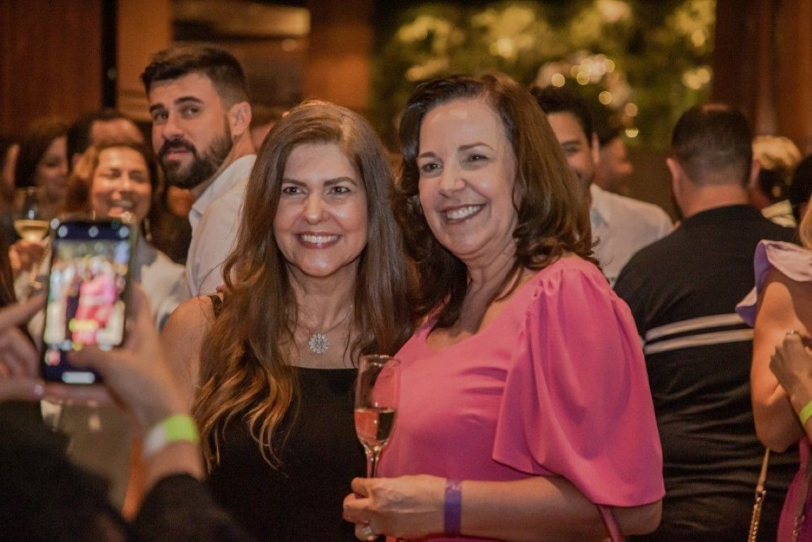 Duas mulheres estão posando para uma foto em uma festa enquanto um homem tira uma foto delas.