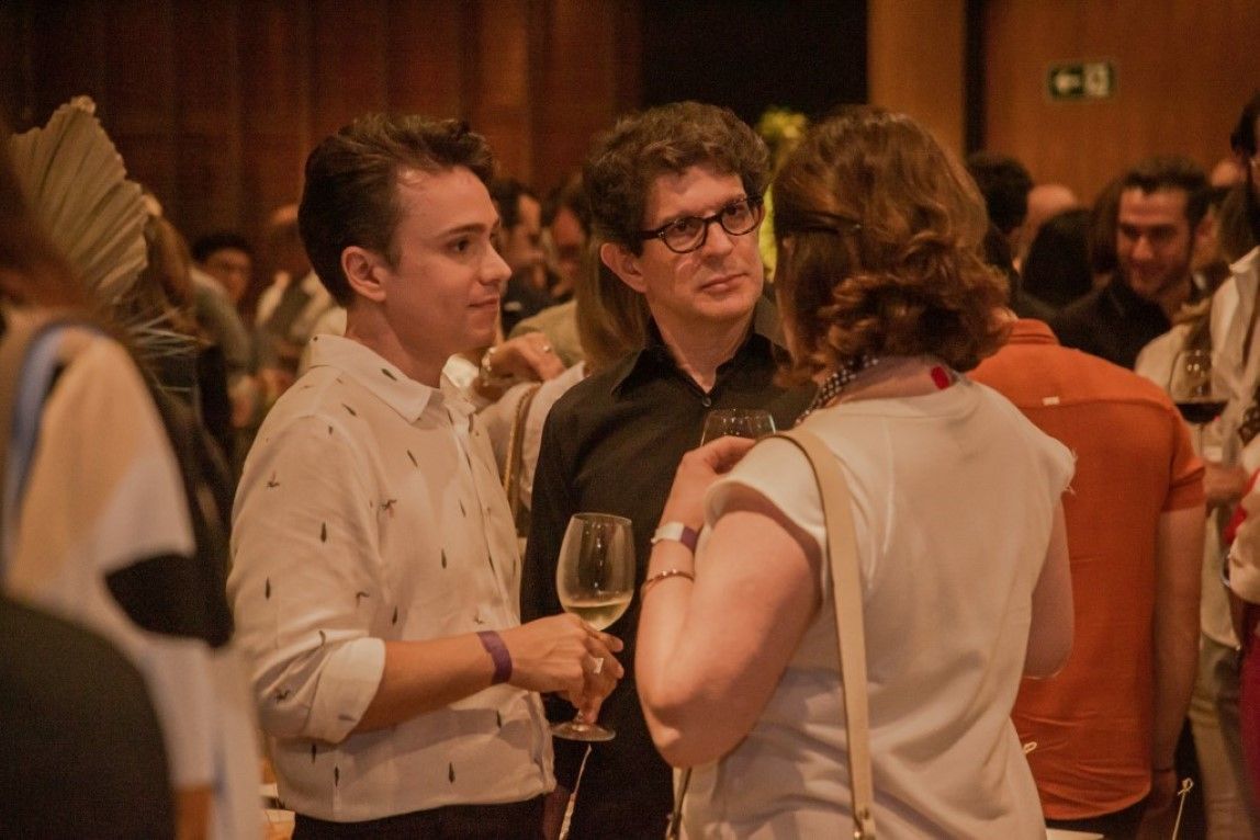 Um grupo de pessoas está em uma sala conversando e bebendo vinho.