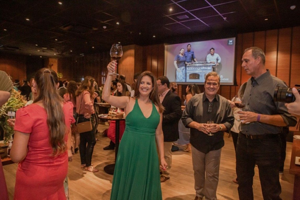 Uma mulher de vestido verde segura uma taça de vinho em uma sala lotada.