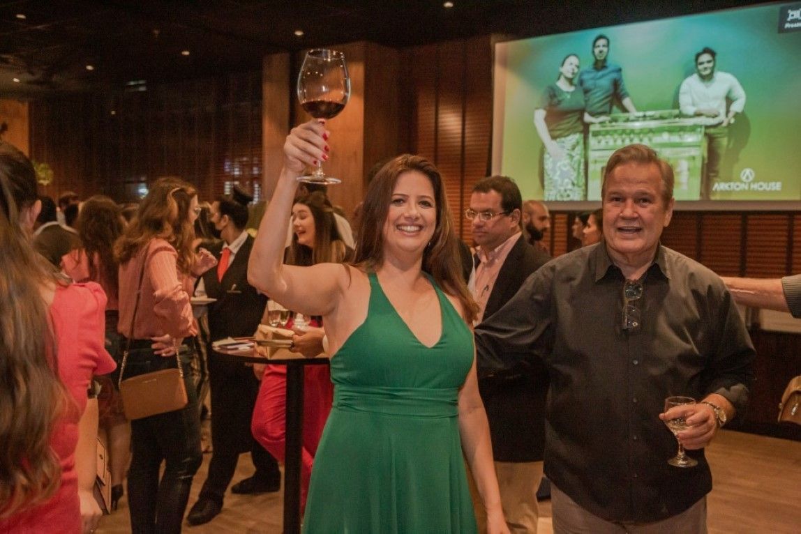 Uma mulher com um vestido verde está segurando uma taça de vinho em uma sala lotada.