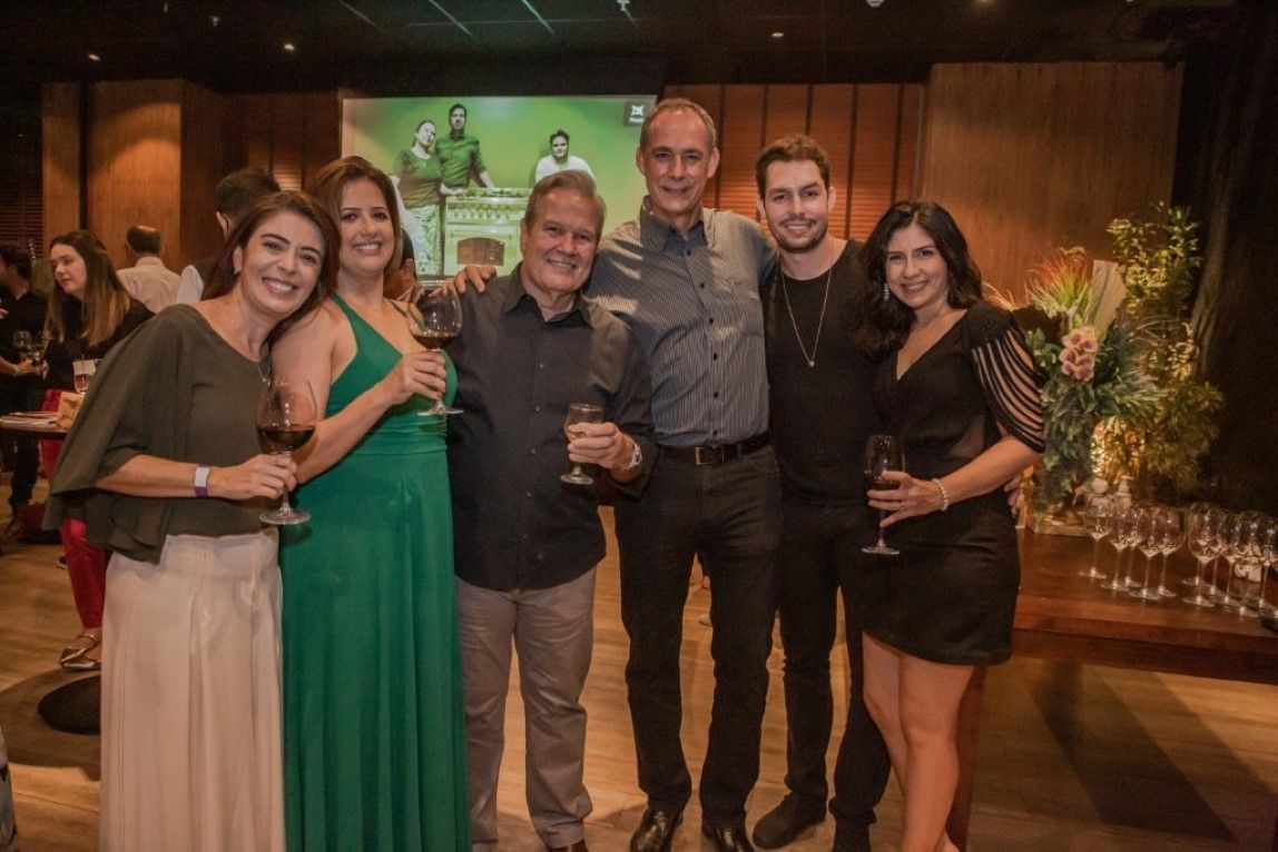 Um grupo de pessoas em pé, uma ao lado da outra, em uma sala, segurando taças de vinho.