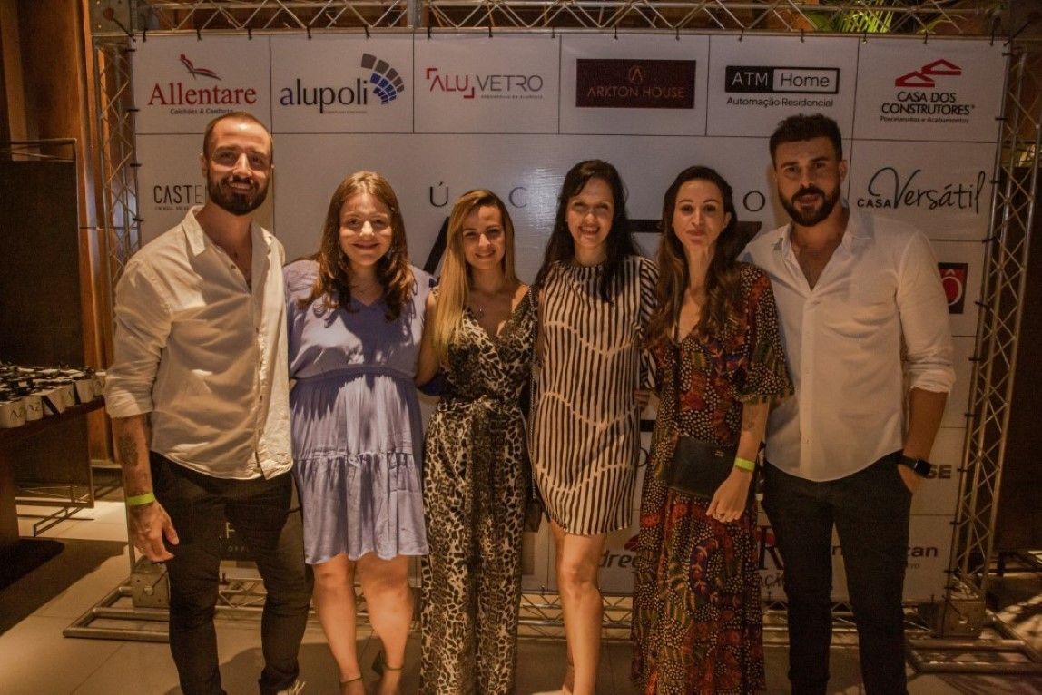 Um grupo de pessoas está posando para uma foto em frente a uma parede com logotipos.