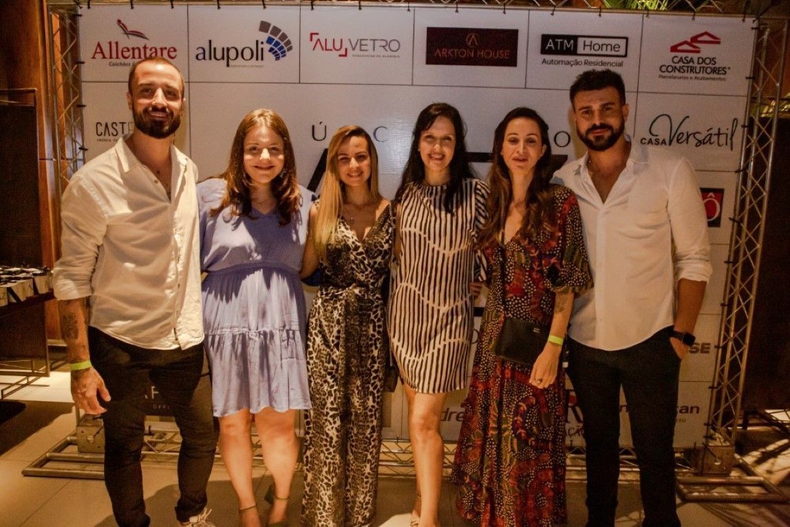 Um grupo de pessoas está posando para uma foto em frente a uma parede com logotipos.