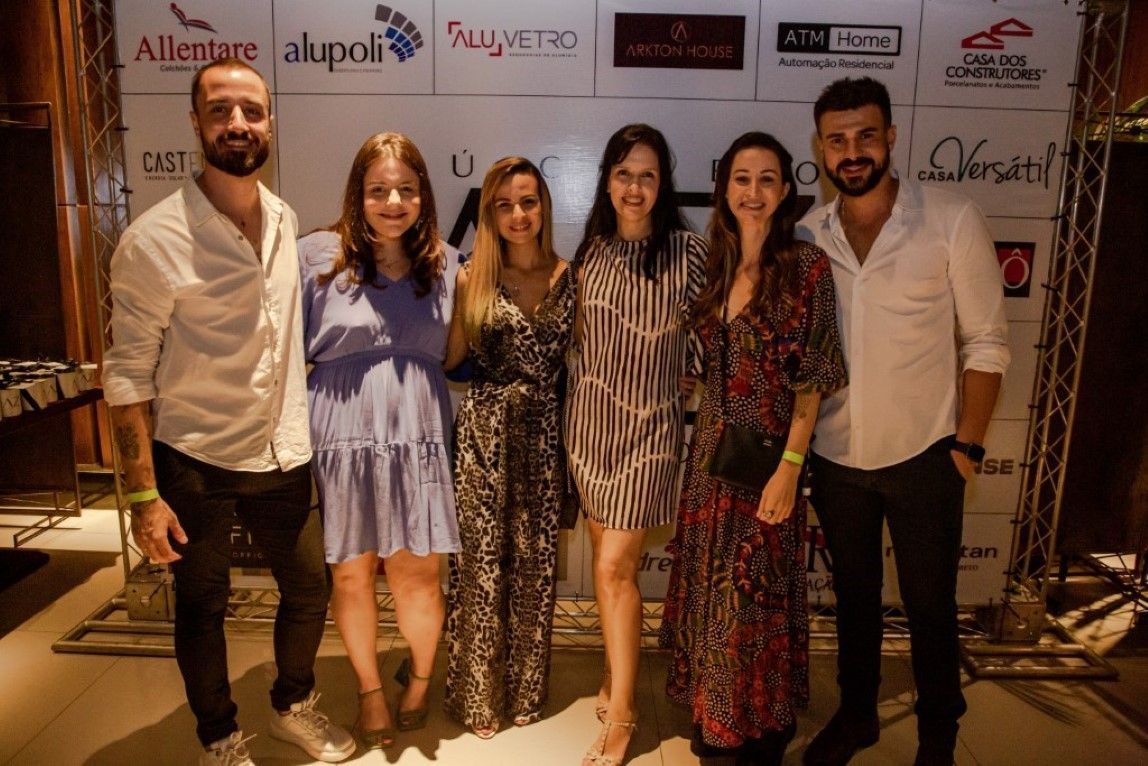 Um grupo de pessoas está posando para uma foto em frente a uma parede com logotipos.