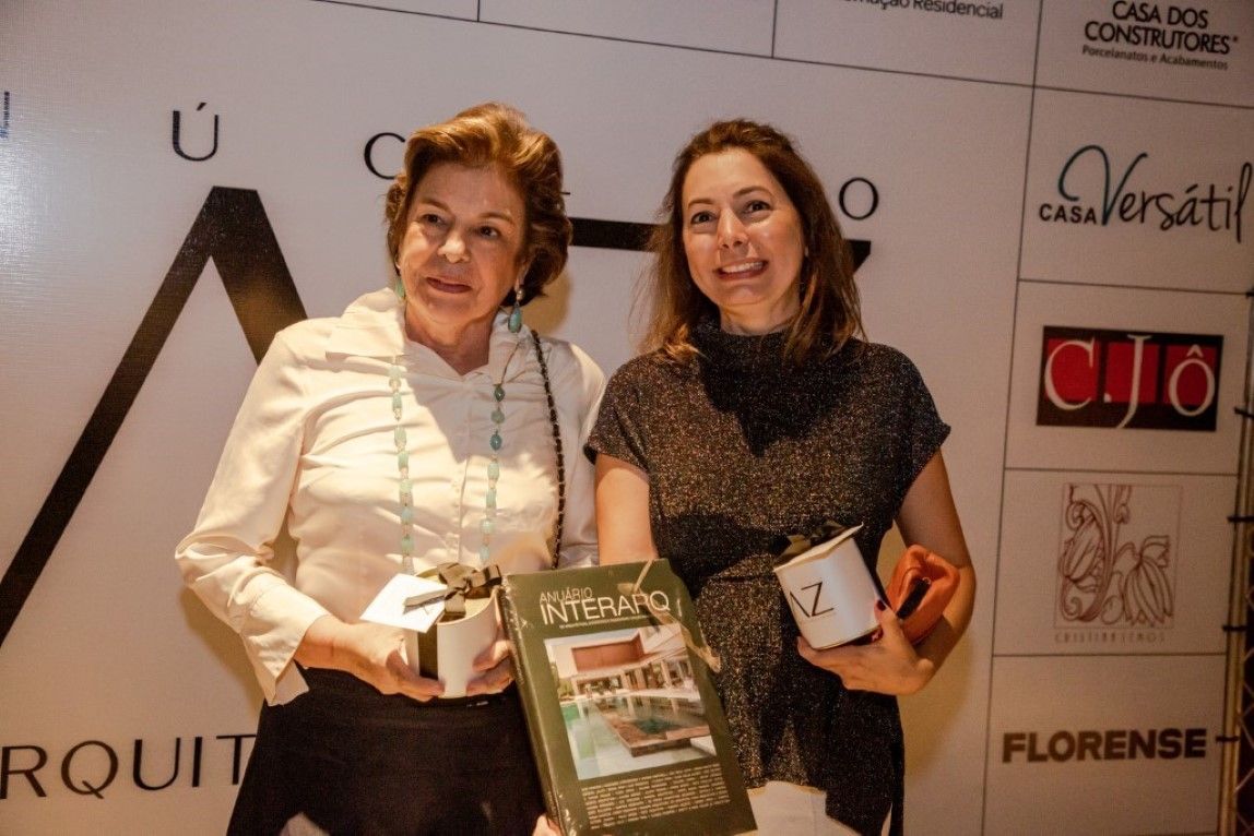 Duas mulheres de pé uma ao lado da outra segurando um livro