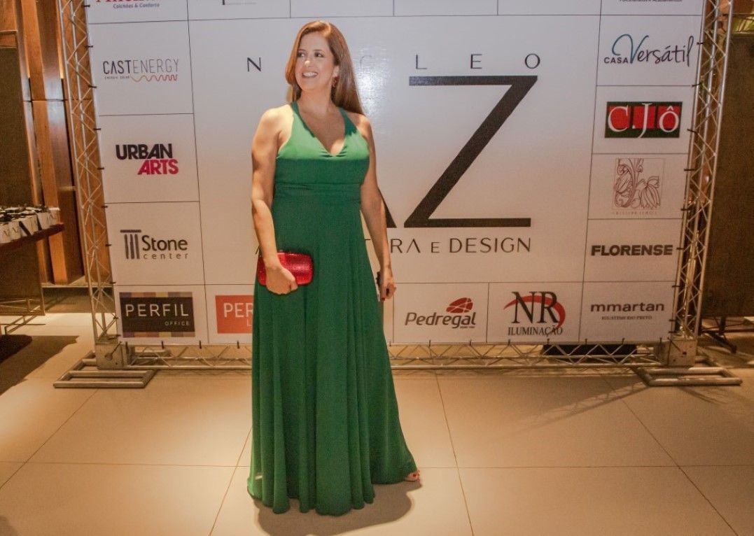 Uma mulher com um vestido verde está parada em frente a uma parede com logotipos.