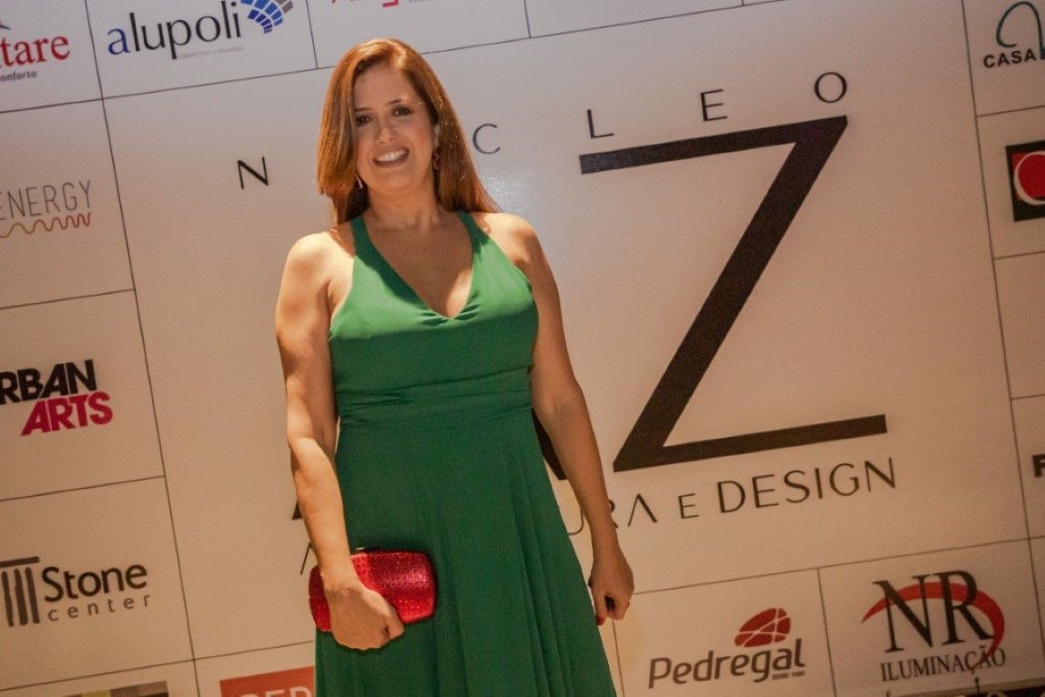 Uma mulher com um vestido verde está em frente a uma parede que diz cleo
