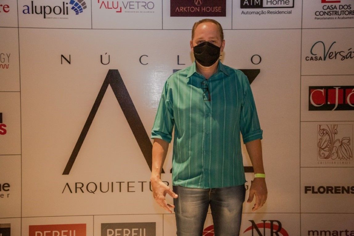 Um homem usando uma máscara está parado em frente a uma parede com logotipos.